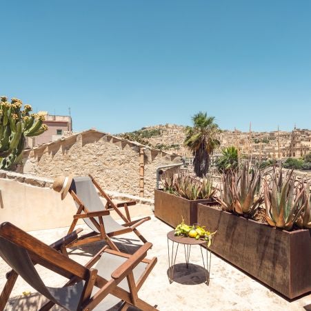 Elegant boutique hotel room with rustic stone walls, minimalist four-poster bed, and warm terracotta tones in a historic Sicilian setting