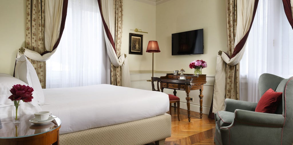 Opulent junior suite with ornate gold-trimmed walls, crystal chandelier, antique furniture and king bed draped in fine Italian linens