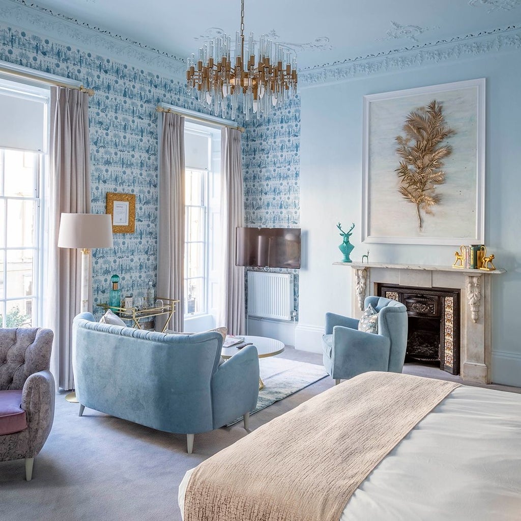 Elegant junior suite with plush king bed, modern gray headboard, soft neutral decor, and large windows overlooking contemporary UK hotel interior