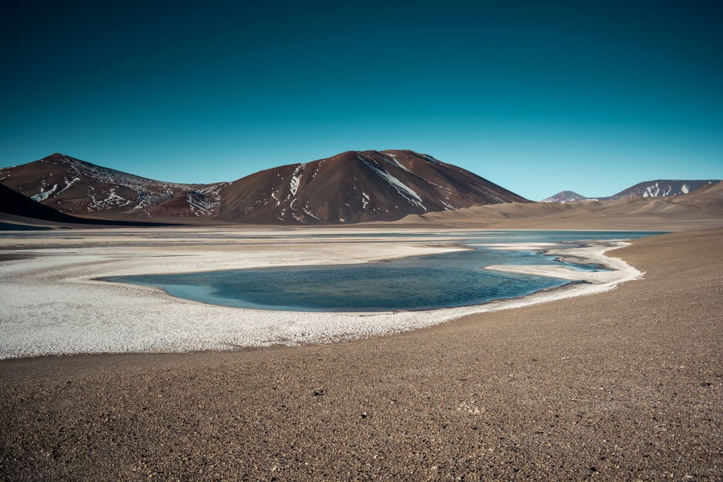 Snow-capped mountains frame an exclusive desert resort with infinity pool overlooking Chile's vast Atacama Desert at golden hour