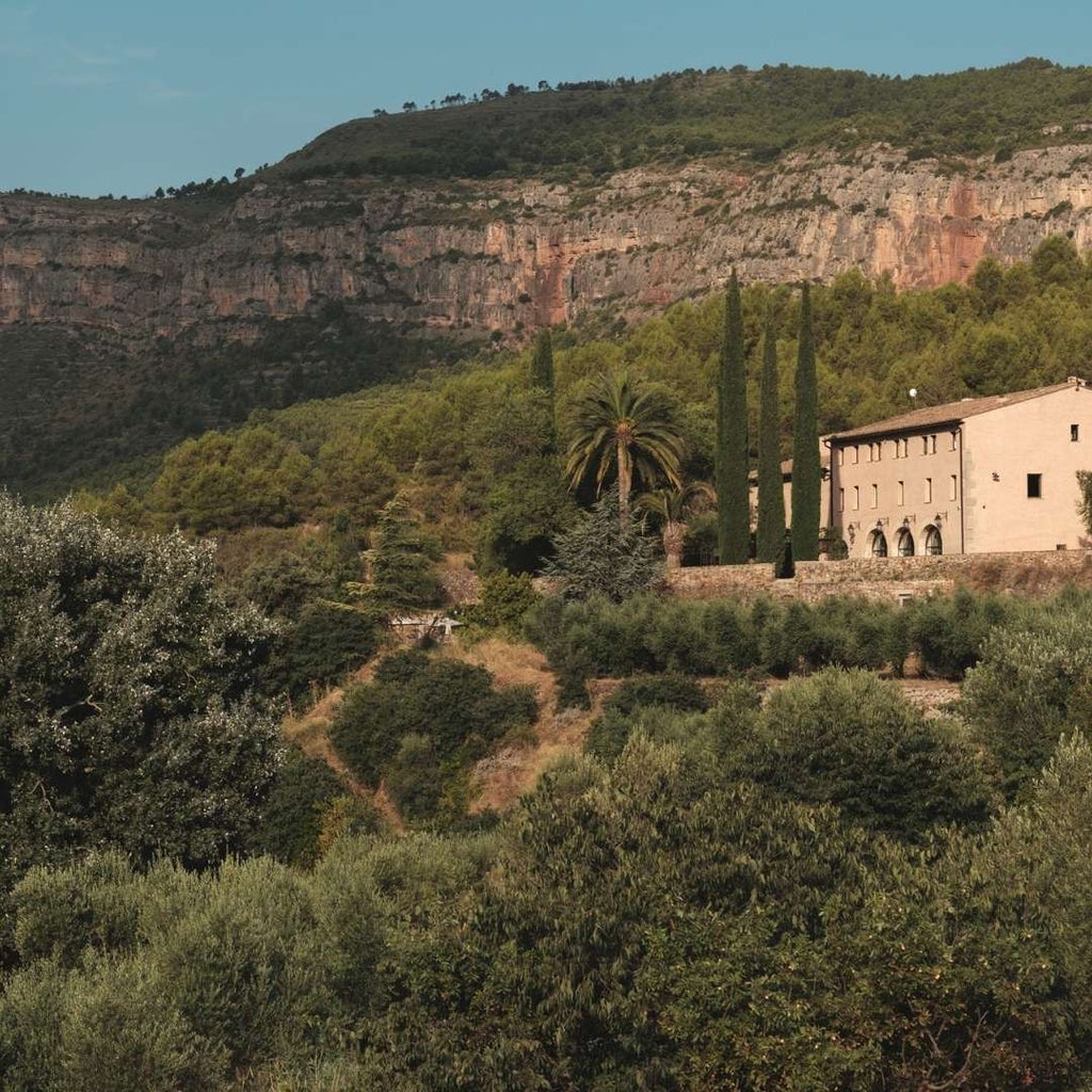 Luxurious Spanish winery hotel nestled among rolling vineyards, featuring stone architecture, elegant terrace, and panoramic mountain landscape at sunset