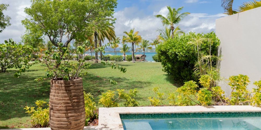 Luxurious beachside suite with private plunge pool overlooking turquoise waters, white sand, and lush tropical landscape at Jumby Bay Island resort, Antigua