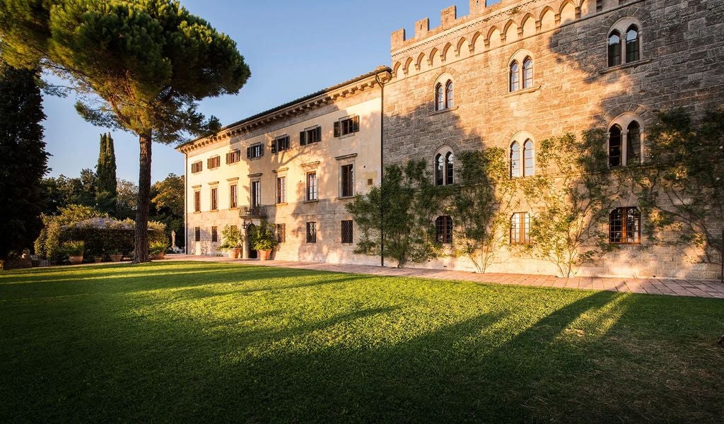 Elegant Tuscan villa with stone facade nestled on hilltop amongst cypress trees, featuring infinity pool overlooking rolling countryside