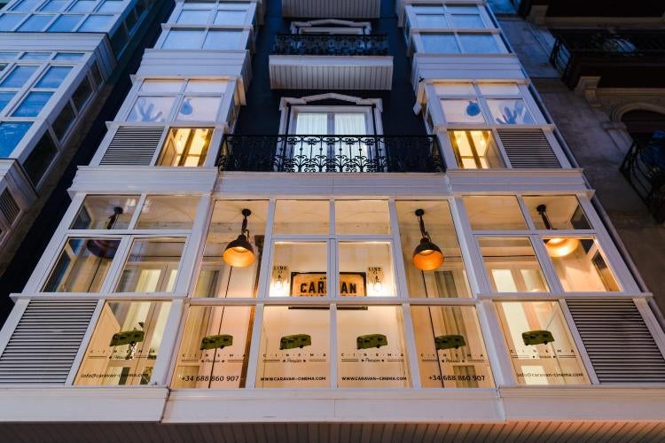 Elegant boutique hotel exterior with white-washed walls, arched windows, and a rustic wooden entrance surrounded by Mediterranean flora