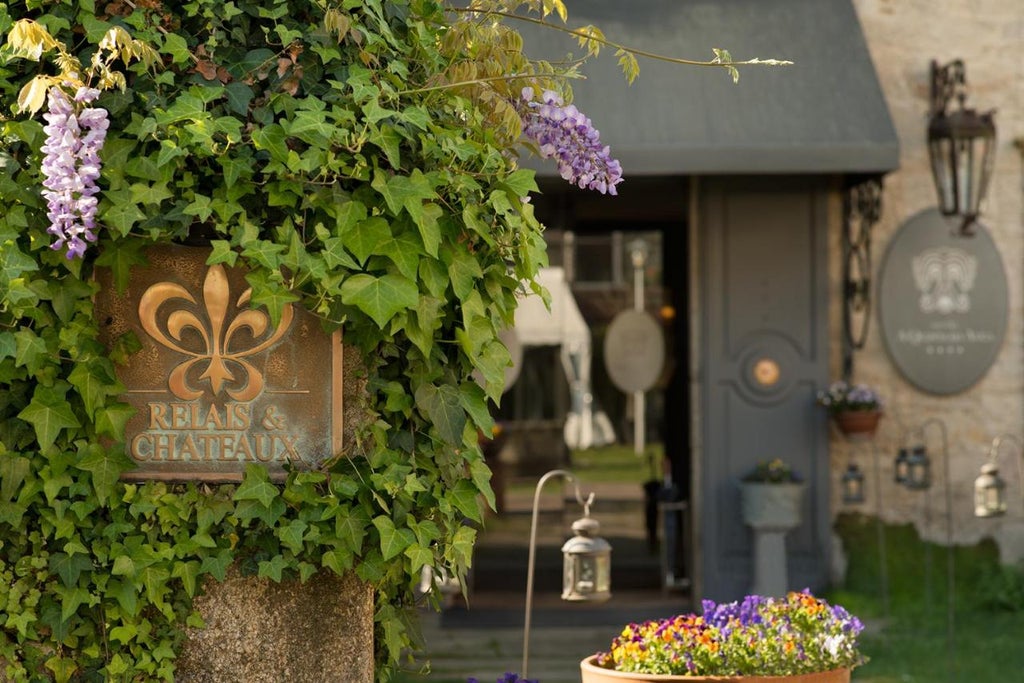 Elegant stone hotel with ivy-covered facade, manicured gardens, and ornate balconies nestled in a lush Spanish countryside setting