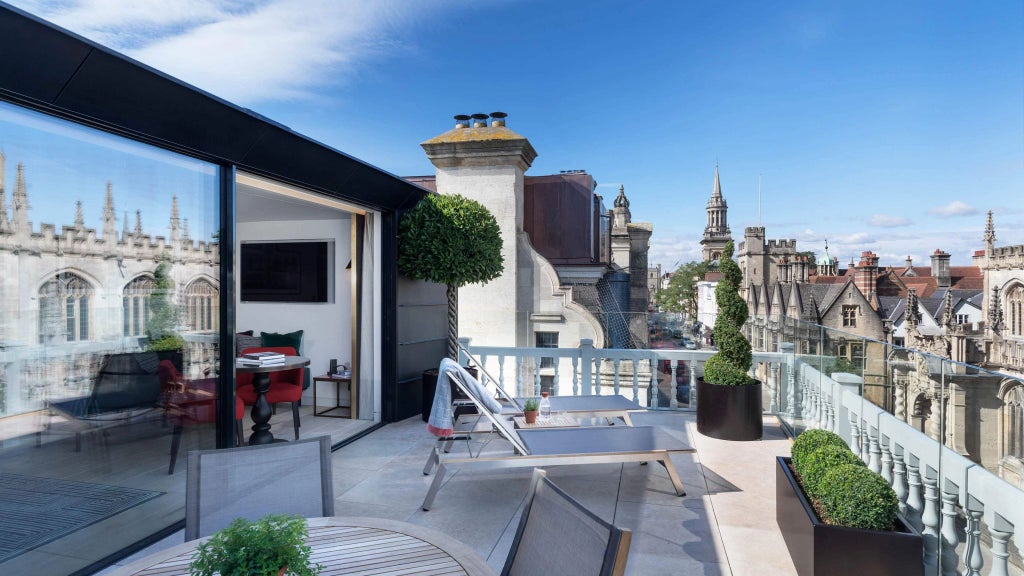 Elegant historic hotel room with large windows overlooking scenic cityscape, featuring classic wooden furnishings and refined British architectural details