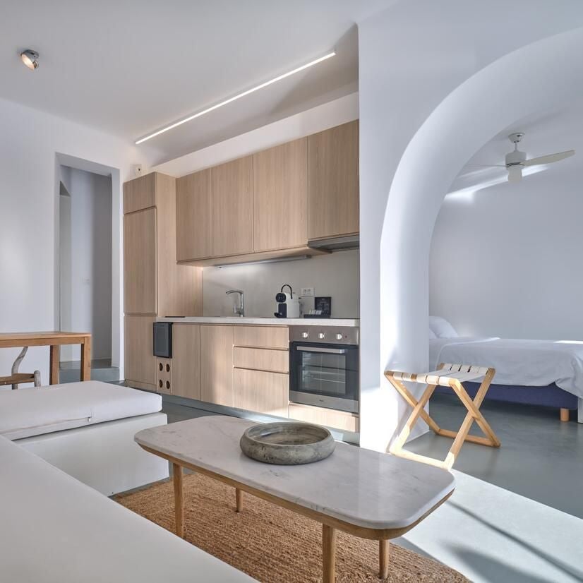 Luxurious white-walled Santorini suite with minimalist decor, blue-domed ceiling, plush king bed, and panoramic Aegean Sea view through arched window