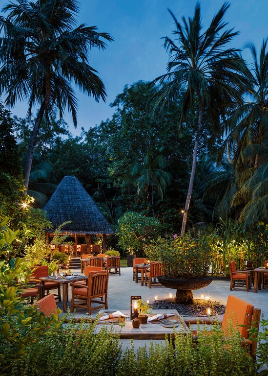 Luxurious overwater villa with infinity pool overlooking turquoise Maldivian lagoon, surrounded by tropical palms at dusk