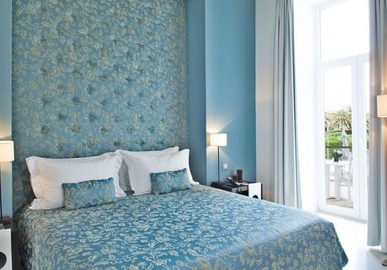 Elegant garden view room at coastal resort, featuring crisp white linens, minimalist design, and lush greenery through expansive windows in Portugal.