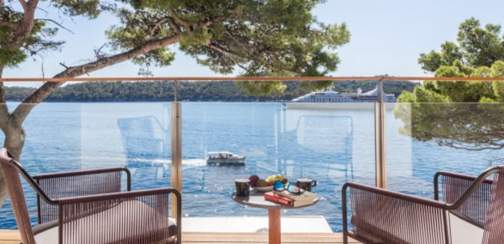 Elegant coastal hotel room with private balcony overlooking Adriatic Sea, featuring modern furnishings and floor-to-ceiling windows