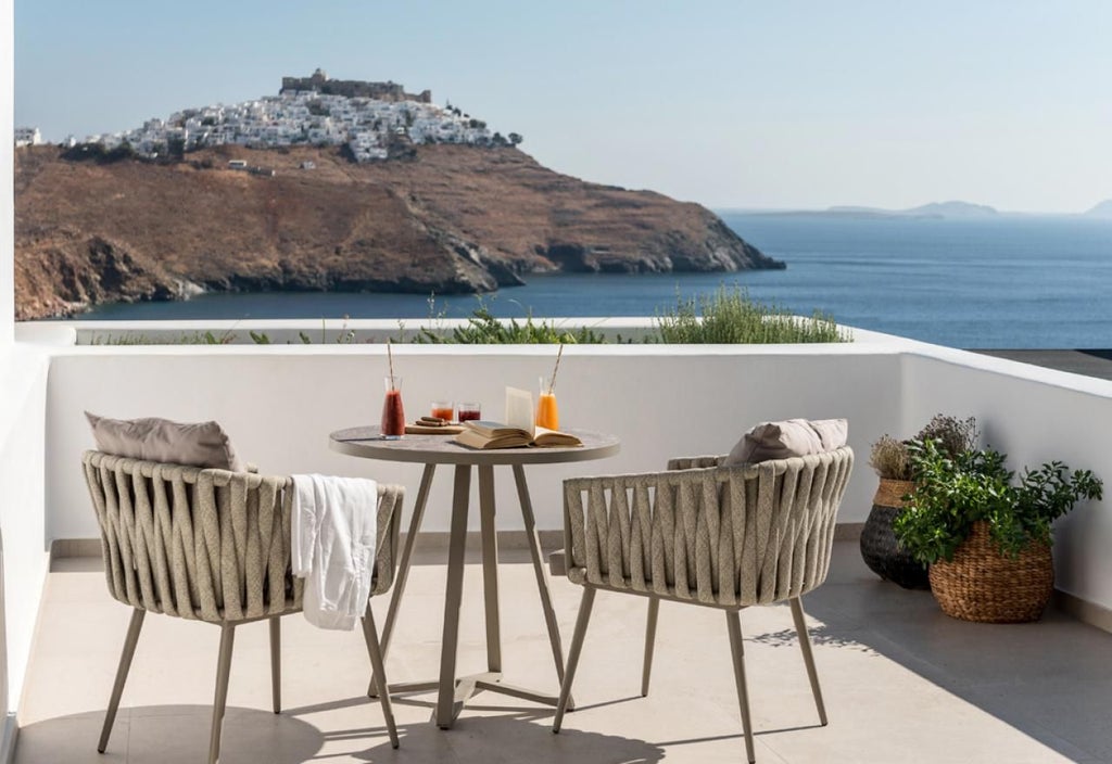 Elegant honeymoon suite in Greece with pristine white walls, minimalist decor, luxurious king bed, and breathtaking Aegean Sea view from private balcony