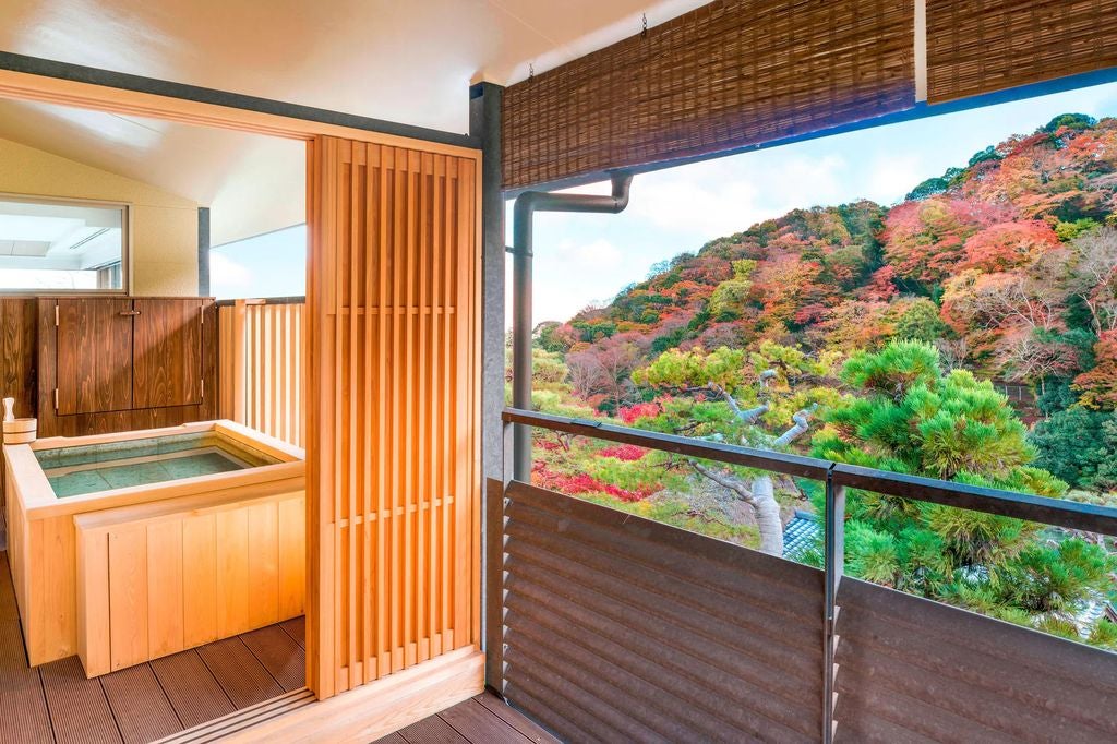 Traditional Japanese ryokan hotel with wooden exterior, serene Zen garden, stone lanterns and flowing stream amid autumn maple trees