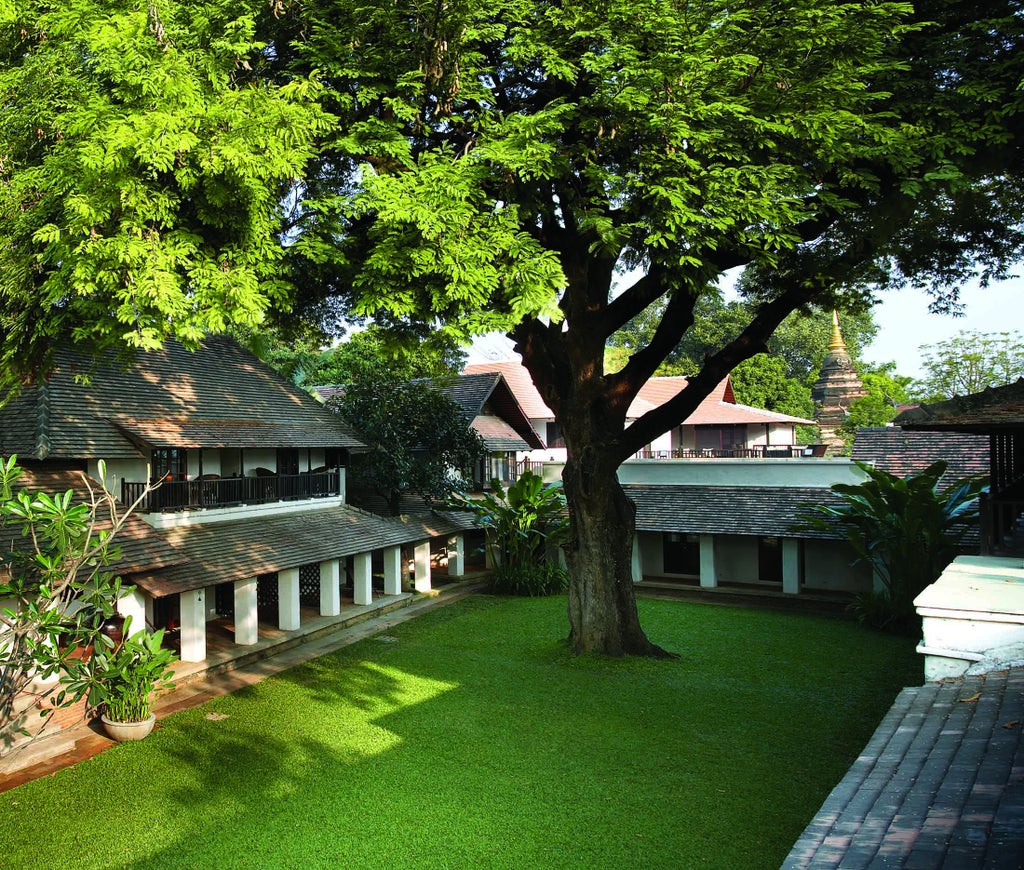 Tranquil boutique hotel courtyard with tropical plants and traditional Thai lanterns lining a stone pathway between wooden buildings