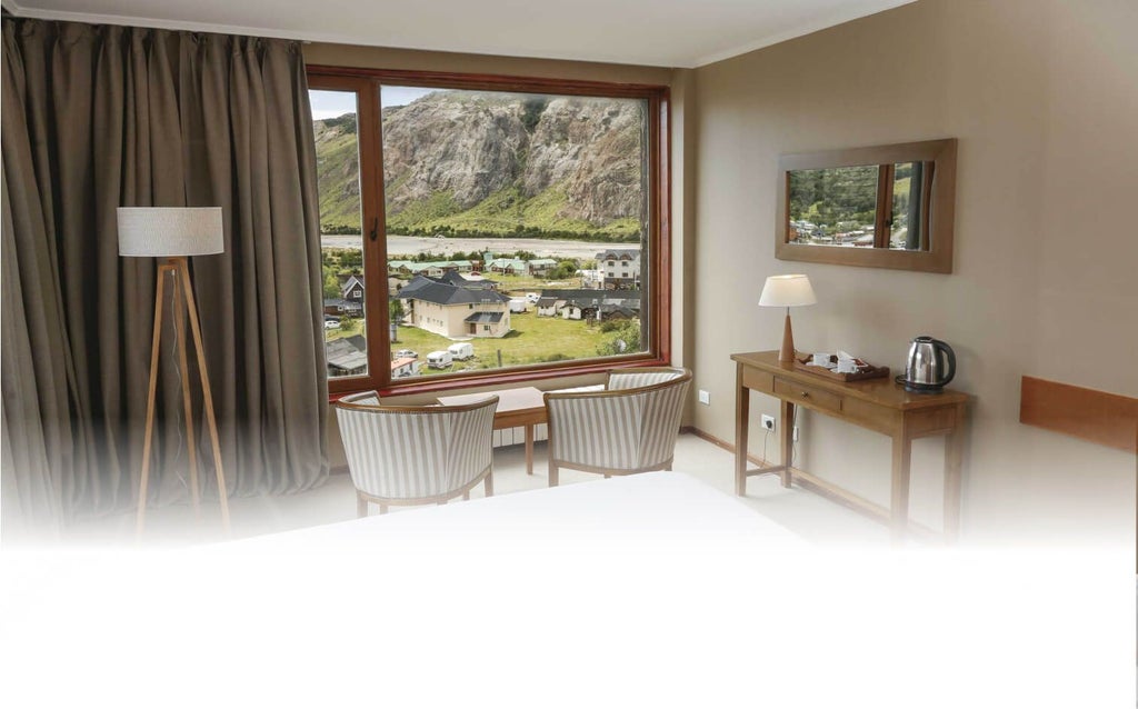 Elegant mountain-view hotel room with rustic wooden accents, plush bedding, and panoramic windows overlooking scenic Patagonian landscape at Los Cerros Boutique Hotel