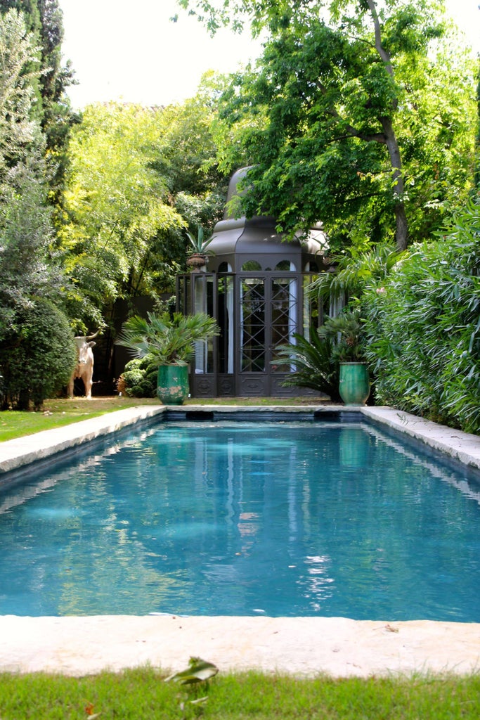 Elegant French boutique hotel courtyard with ornate stone fountain, lush gardens, cream facade and wrought iron balconies at dusk