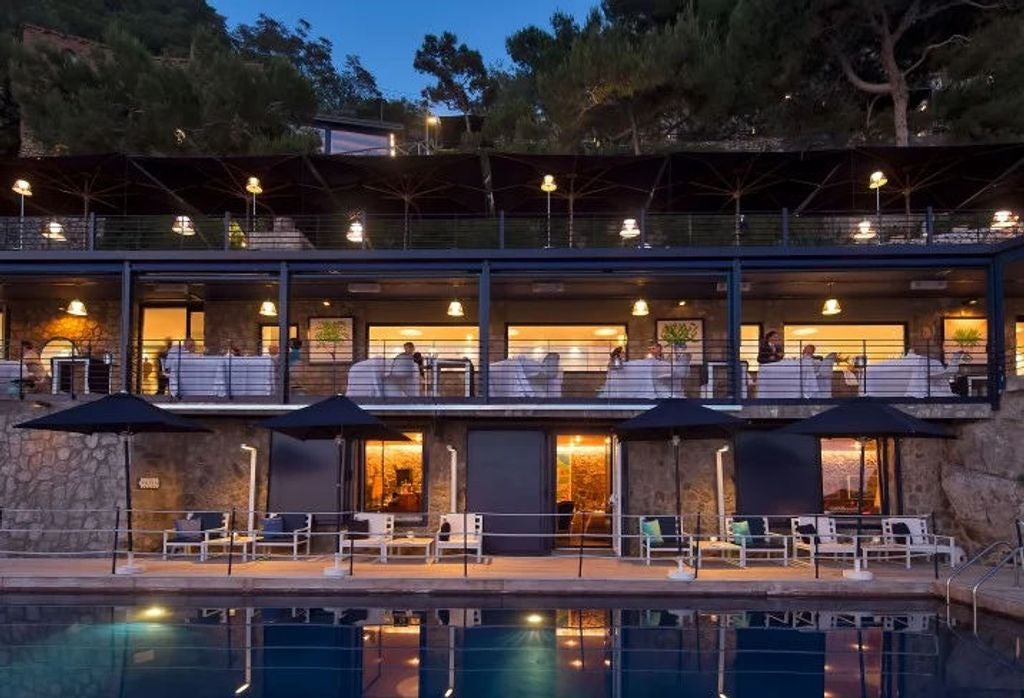 A luxurious seaside hotel balcony overlooking the Mediterranean, featuring a private plunge pool and elegant lounge chairs against rocky cliffs