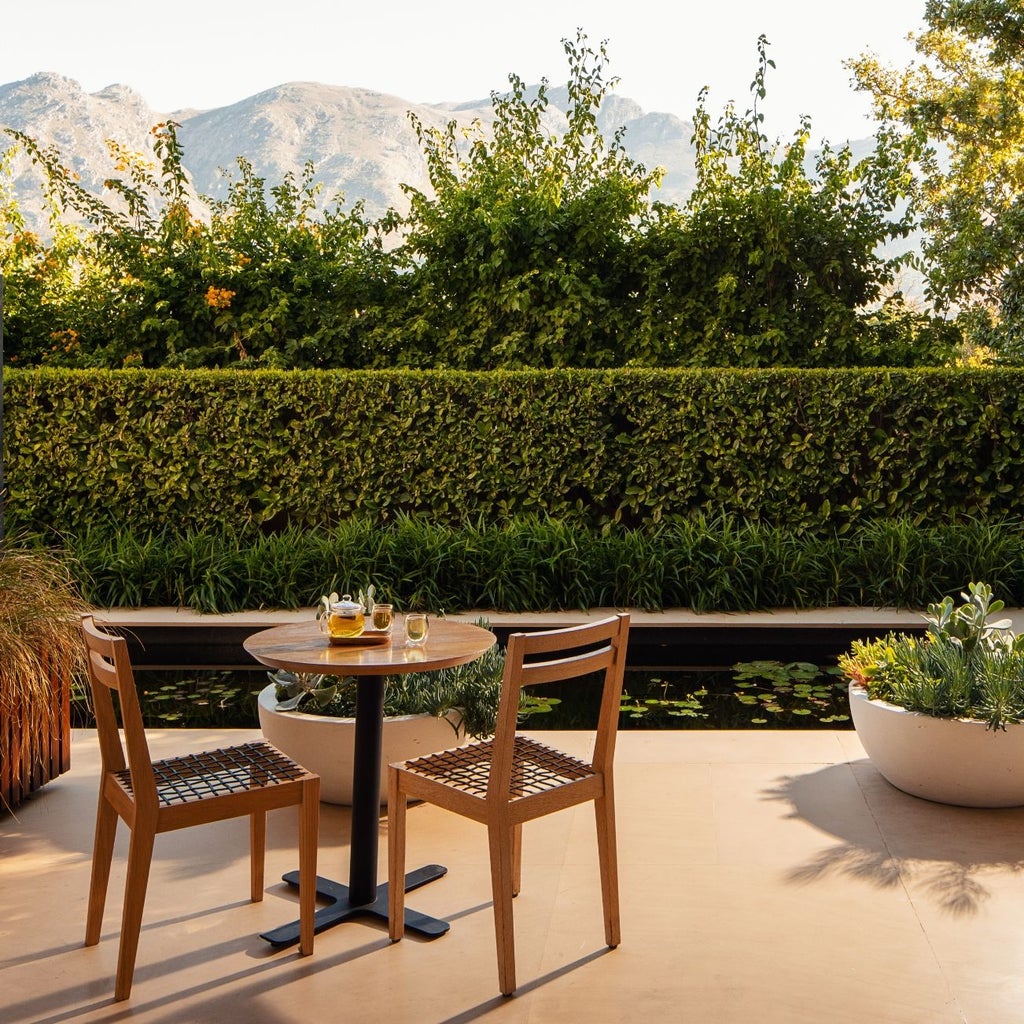 Elegant boutique hotel nestled in South African wine country, featuring white-washed buildings, lush gardens, and a serene courtyard with verdant landscaping.