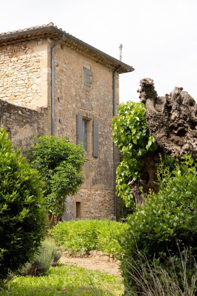 Elegant stone farmhouse hotel nestled in Provençal countryside, featuring lavender fields, rustic stone walls, and soft golden sunlight filtering through cypress trees