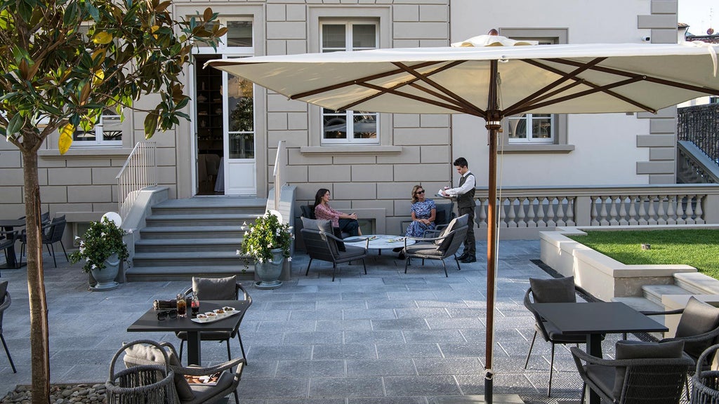 Elegant Italian boutique hotel facade with stone walls, arched windows, and lush greenery, nestled in a picturesque historic urban landscape at sunset