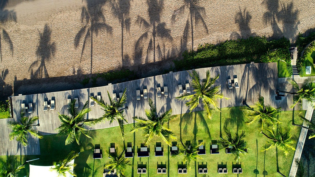 Modern luxury beachfront villa with infinity pool overlooking Bali Sea, glass walls, teak deck, and overwater sunbeds at sunset