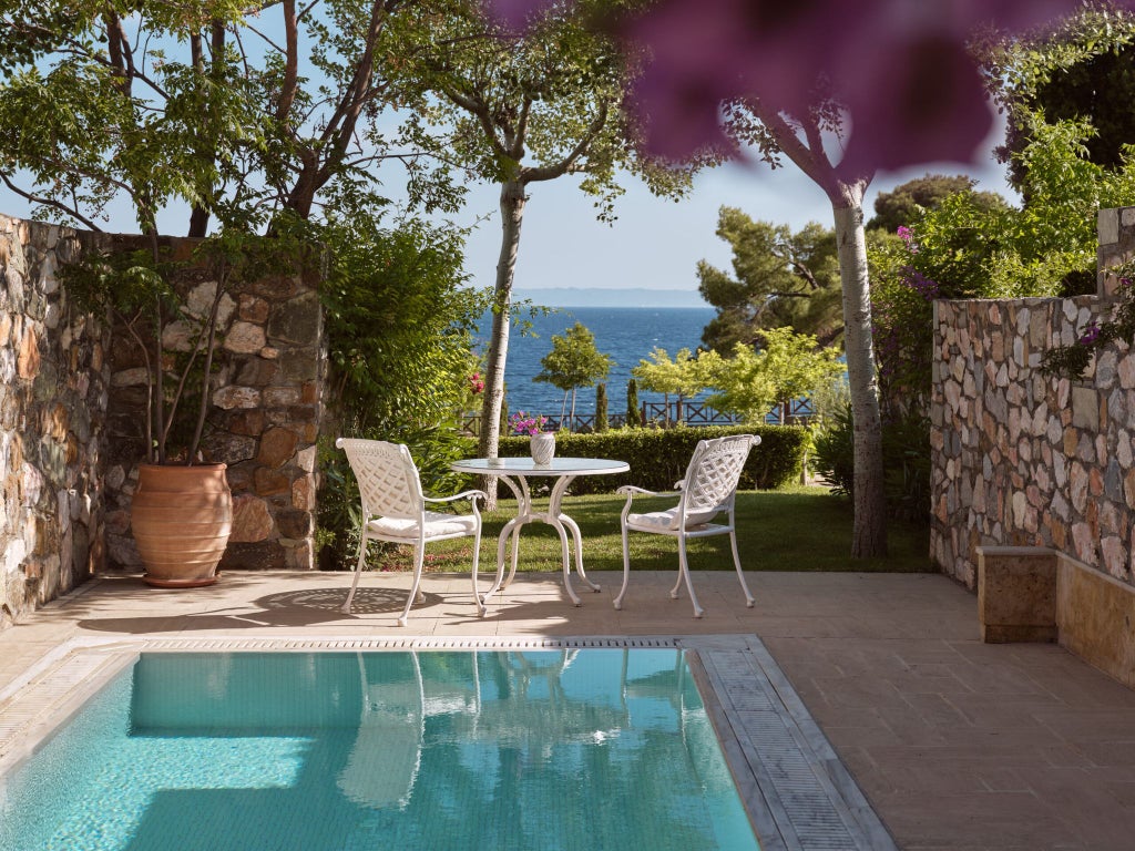 Luxurious pool suite with private pool overlooking azure Aegean waters, featuring elegant modern Greek design and sun-drenched outdoor terrace at seaside resort