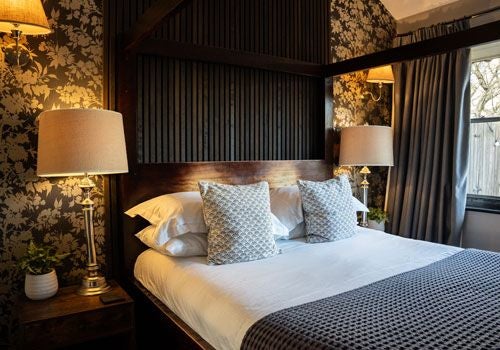 Elegant boutique hotel room with plush white bedding, soft neutral tones, and expansive window overlooking scenic countryside near Yorkshire Dales