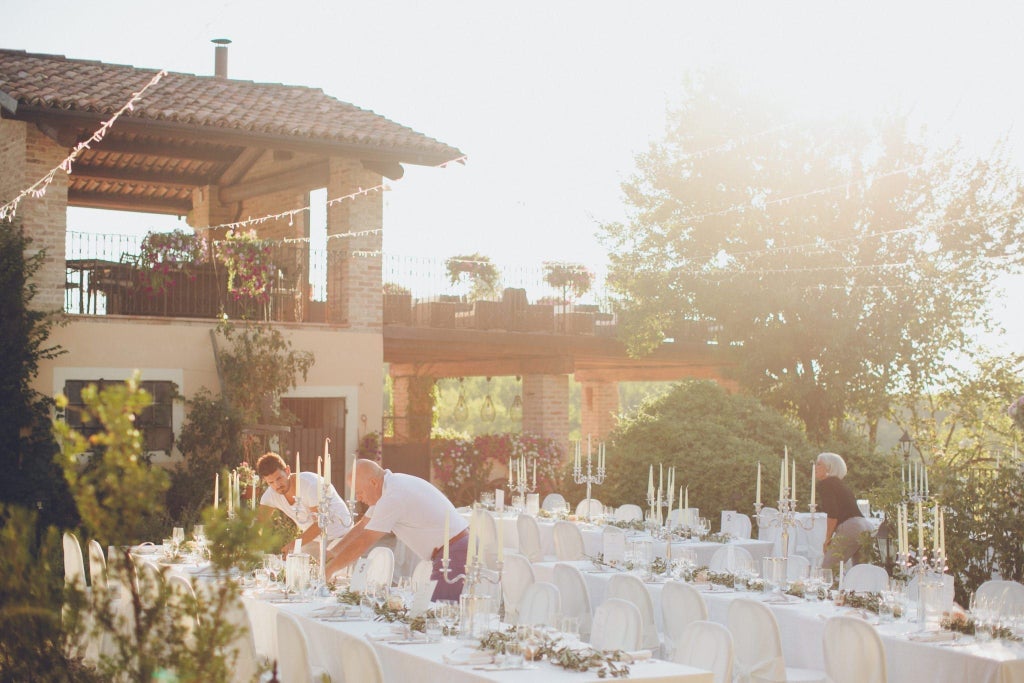 Elegant Italian coastal hotel with white stucco facade, blue shutters, lush gardens, and panoramic Mediterranean Sea view at sunset