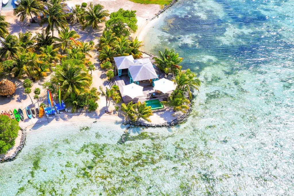 Private beachfront villa with thatched roof and wooden deck overlooking turquoise Caribbean waters at sunset in Belize