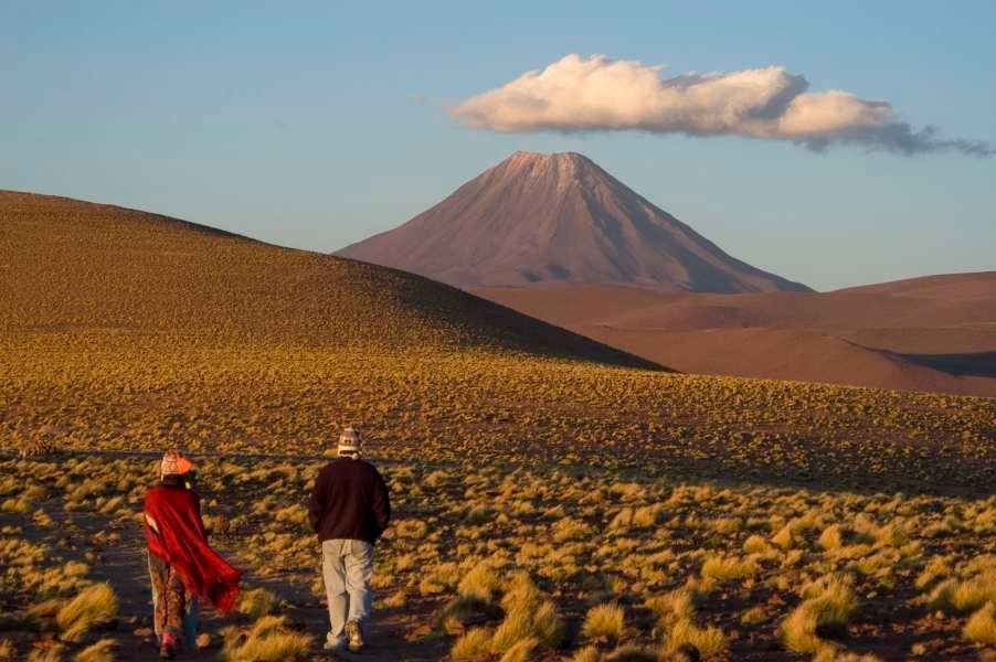 Luxury desert lodge with adobe walls nestled against red mountains, featuring an infinity pool reflecting the Chilean desert sunset