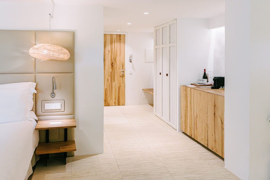 Elegant white-washed Spanish hotel room with minimalist design, natural light, and rustic stone wall, showcasing stunning Menorcan countryside views