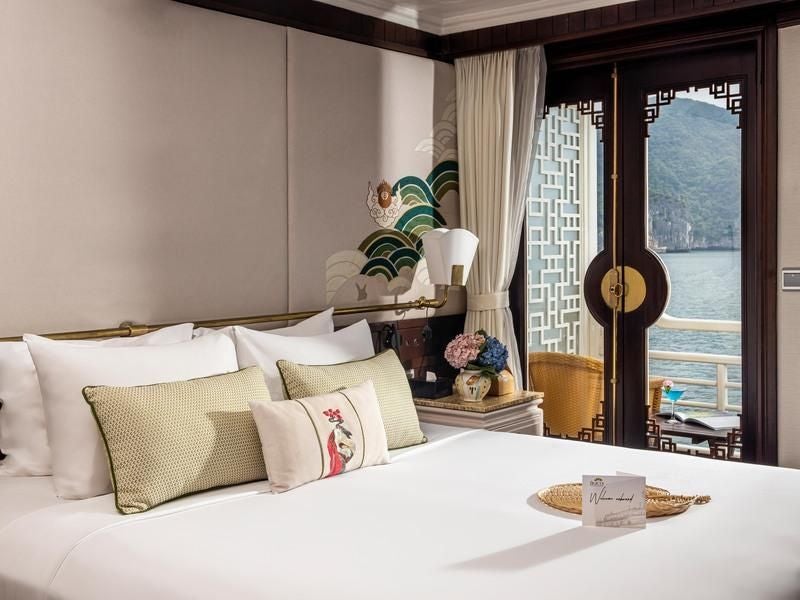 Luxurious executive cabin aboard Bhaya Cruises, featuring elegant wooden furnishings, crisp white linens, and panoramic views of Halong Bay's scenic landscape