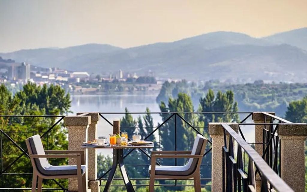 Elegant hilltop resort overlooking Douro Valley vineyards, featuring terracotta roofs and infinity pool amid lush landscaping