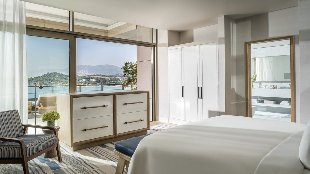 Elegant waterfront suite with floor-to-ceiling windows, modern furnishings, and panoramic views of the Aegean Sea at golden hour