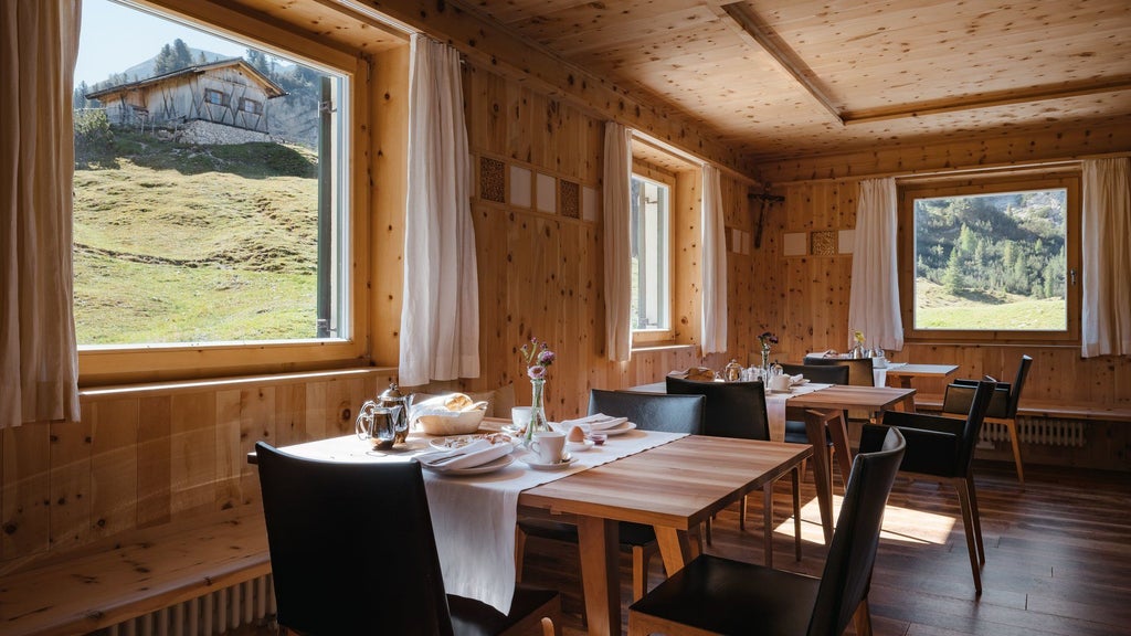 Rustic mountain lodge with wooden balconies nestled in green Alpine meadows, dramatic Dolomite peaks rising in the background