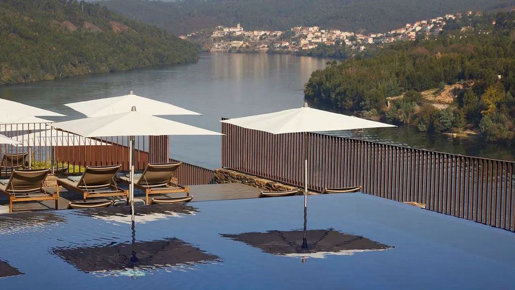 Sleek infinity pool overlooking terraced vineyards of Douro Valley, with modern lounge chairs and panoramic views of the winding river