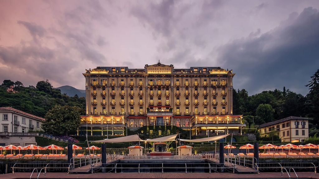 Historic luxury hotel with golden facade overlooking Lake Como, featuring manicured gardens and elegant terraces at sunset