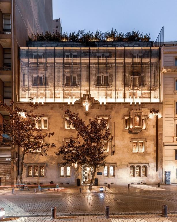 Historic boutique hotel with white stone facade, wrought iron balconies, and arched windows set against lush gardens in Santiago's urban center