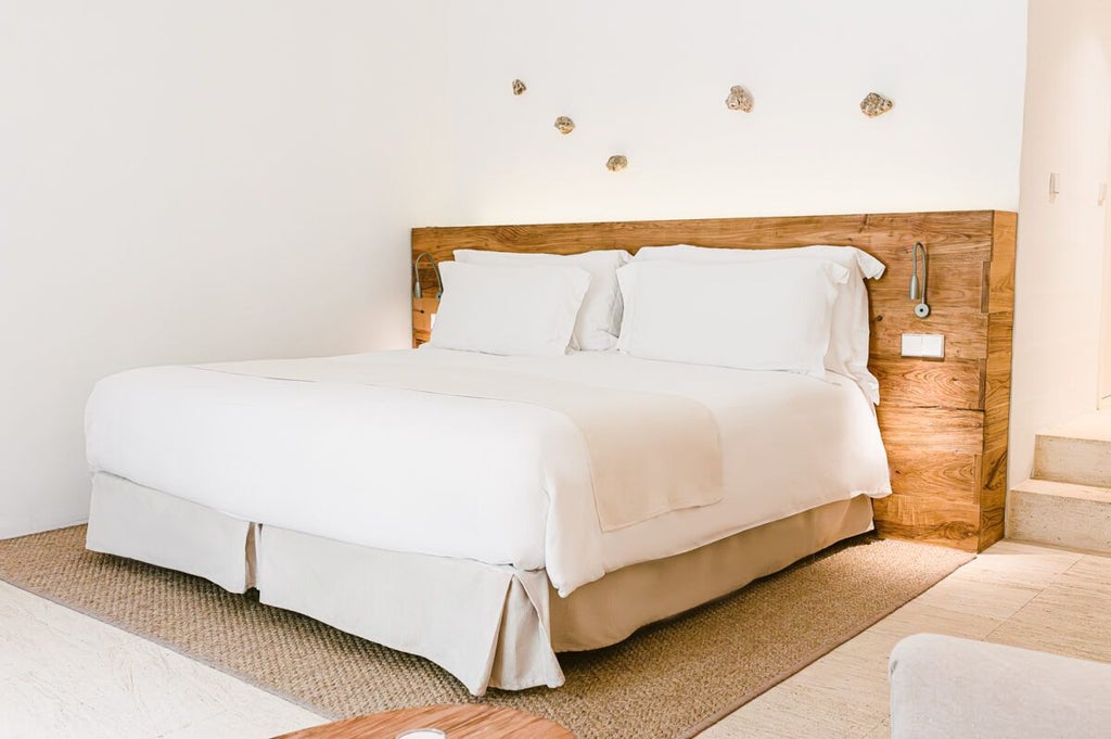 Elegant white-walled hotel room at Torralbenc with minimalist design, crisp linens, wooden accents, and panoramic view of Spanish countryside landscape