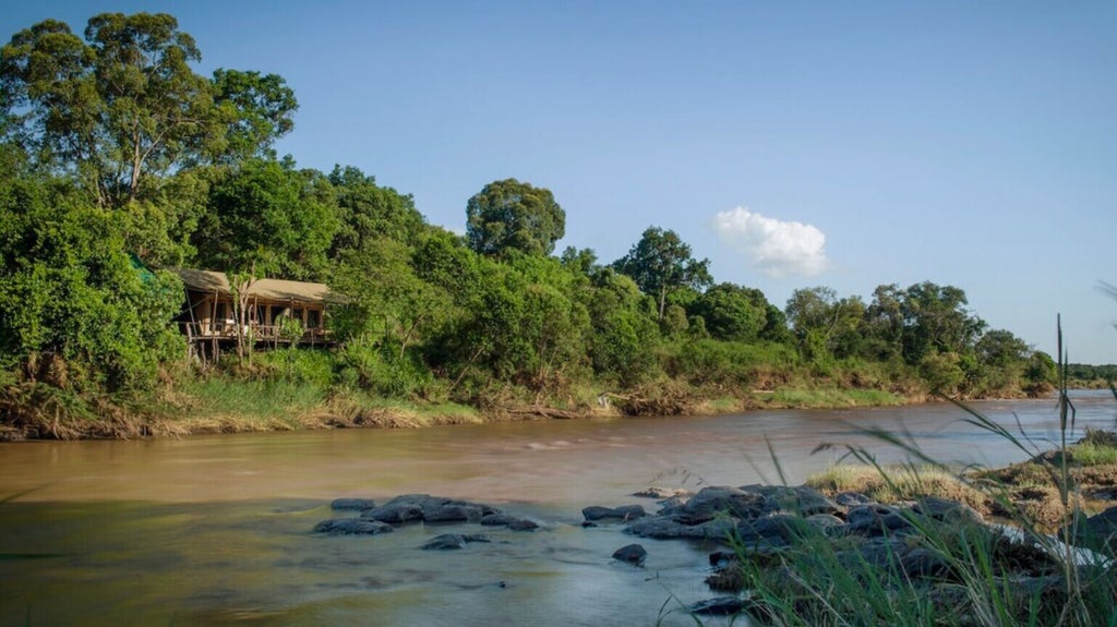 luxurious safari tent overlooking Mara River, expansive canvas veranda with elegant lounge furniture, surrounded by African savanna