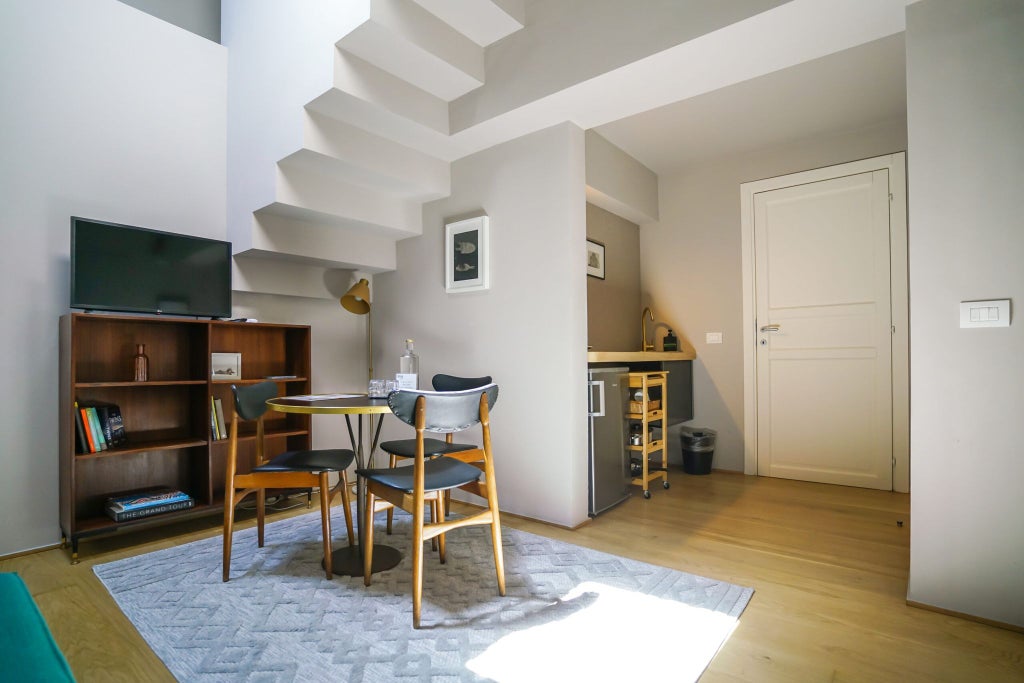 Elegant Italian junior suite with modern minimalist design, warm wood tones, sleek furniture, and soft natural light streaming through large windows