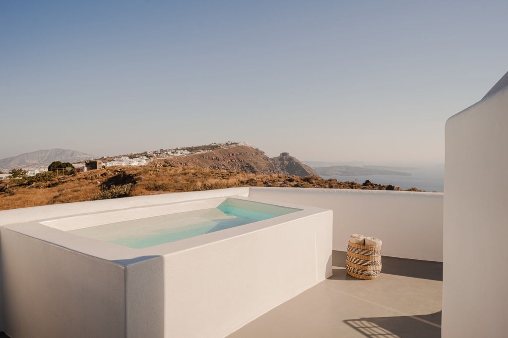 Luxurious white suite overlooking Santorini's caldera, featuring private infinity pool, sundeck loungers and panoramic Aegean Sea views