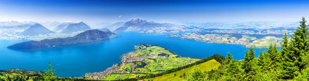 Scenic Swiss Alpine hiking trail overlooking crystalline Lake Lucerne, with snow-capped mountains and lush green meadows framing an elegant trekking experience