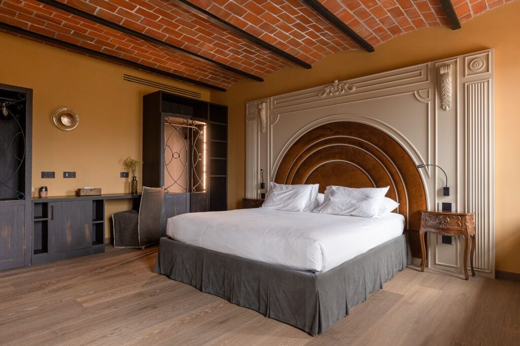 Luxurious minimalist hotel room with soft neutral tones, elegant piano, and expansive garden view in historic Italian boutique resort setting