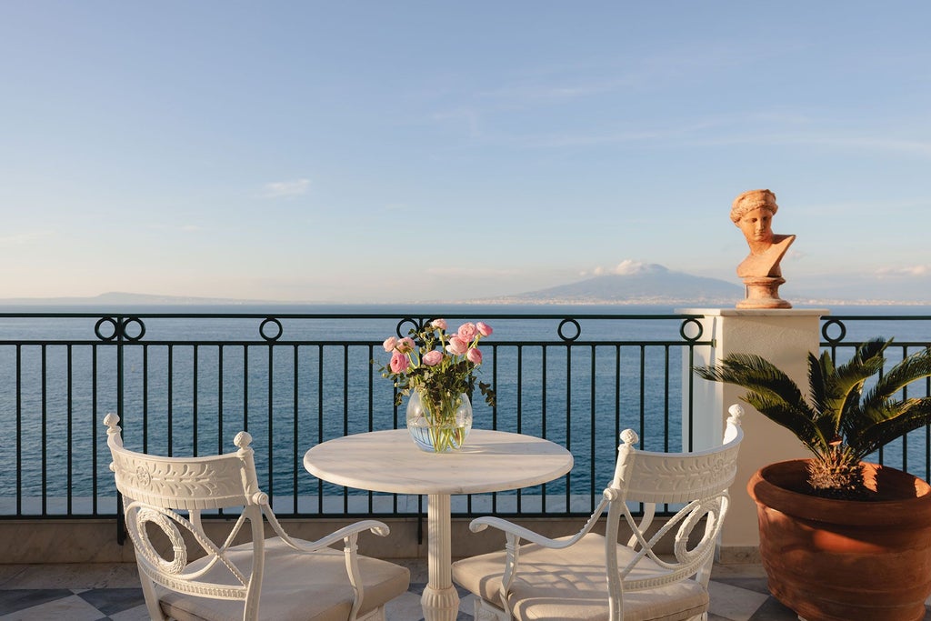 Elegant marble-floored suite with panoramic Sorrento coastline view, ornate crystal chandelier, classic antique furnishings, and plush white king-size bed