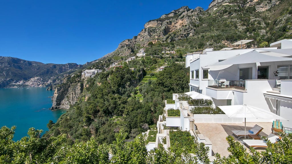 Minimalist white luxury boutique hotel perched on Amalfi Coast cliffs, featuring sleek design, panoramic Mediterranean Sea views, and elegant terraced architecture