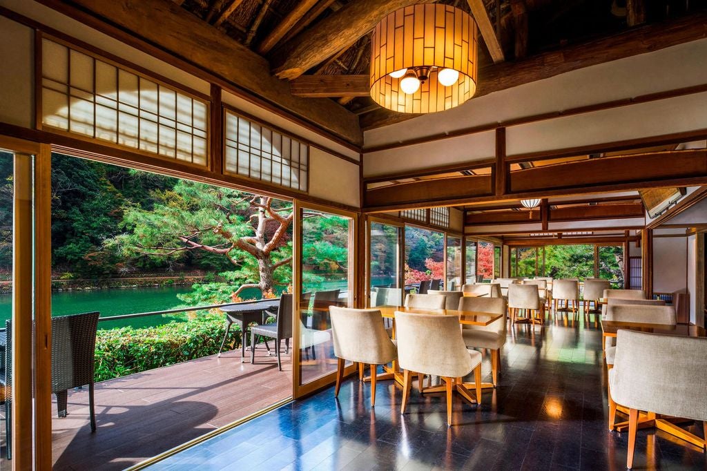 Traditional Japanese ryokan hotel with wooden architecture nestled among vibrant autumn trees beside tranquil Katsura River in Kyoto