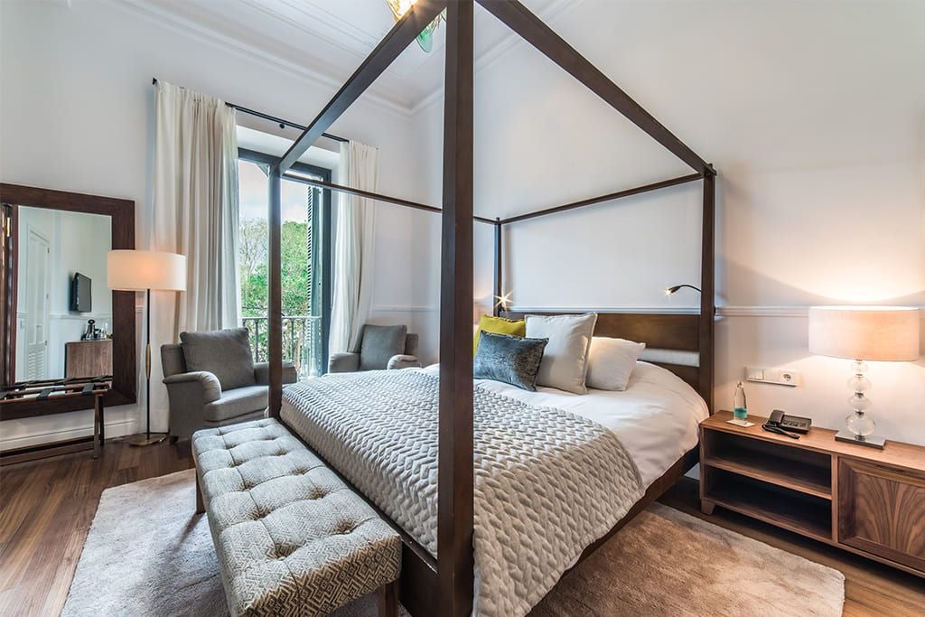 Modern double hotel room with elegant green and white decor, plush bed, garden view, wooden furnishings, and soft natural lighting in a luxurious Spanish countryside retreat.