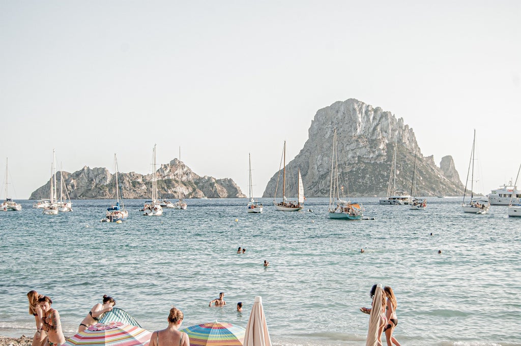 Aerial view of sun-drenched Ibiza coastline featuring white Mediterranean villas, crystal-clear turquoise waters, and luxury yachts