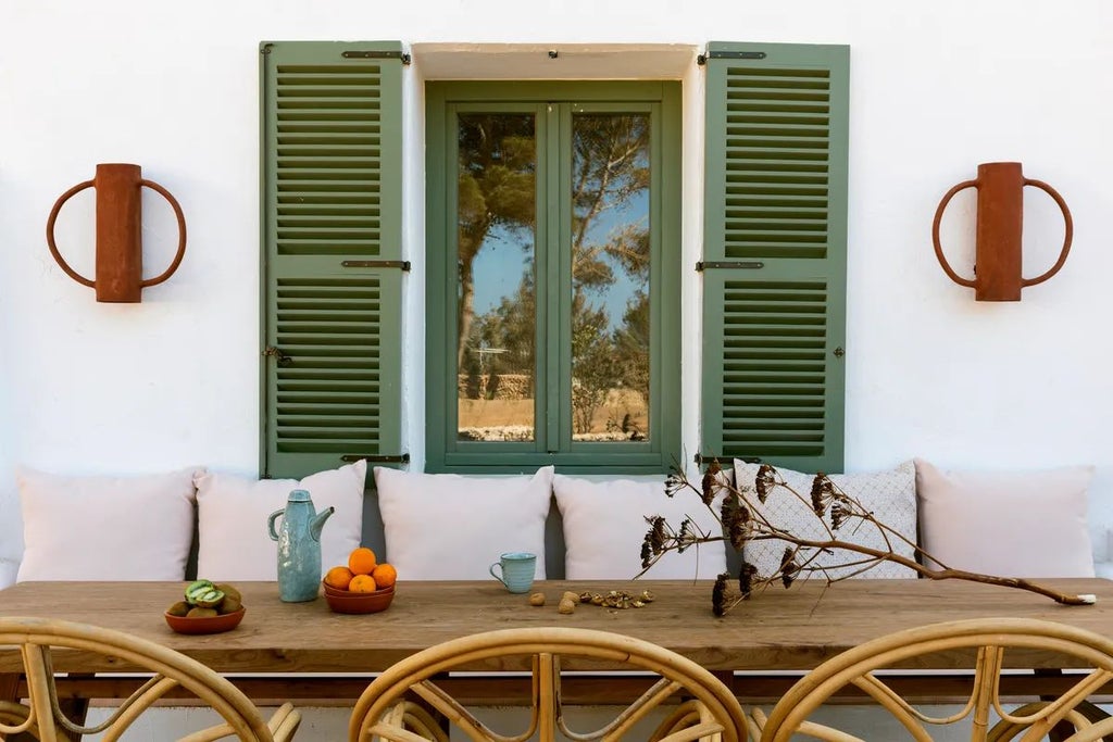 Elegant white-washed Mediterranean hotel with arched windows, terracotta roof, lush greenery, and sun-drenched courtyard in Menorca, Spain