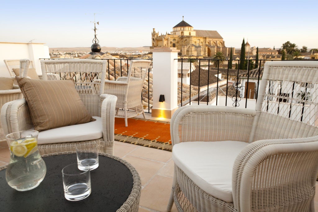 Elegant white-washed Andalusian hotel with ornate balconies, traditional arched windows, and lush courtyard garden in historic Córdoba, Spain